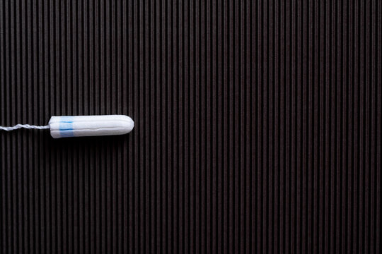 top view of cotton hygienic tampon on black textured background.