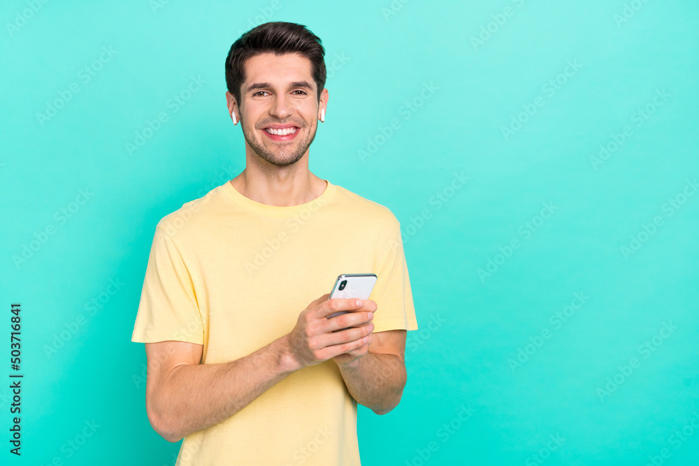 Wall mural Photo of cute brunet millennial guy hold telephone wear t-shirt headphones isolated on teal color background