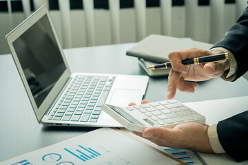 Young Asian businessman hand pressing a calculator to calculate, analyze, graph, finance, income...