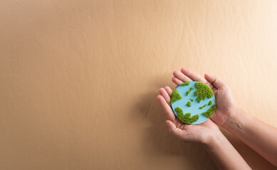 Hands holding paper earth with grass on brown background. World environment day, earth day and save earth concept.