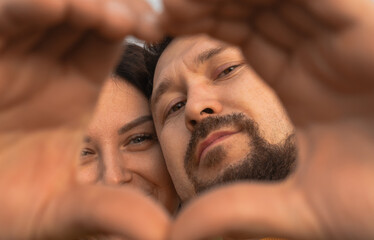 Happy excited couple portrait with hand heart shaped frame. Young man and woman in love having fun, looking at camera and smiling