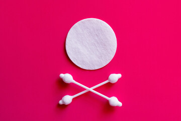 crossed ear sticks under white cotton pad on pink background, top view.