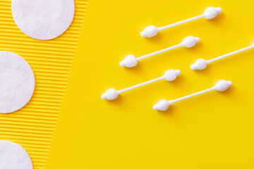 top view of hygienic ear sticks and cosmetic cotton pads on yellow textured background.