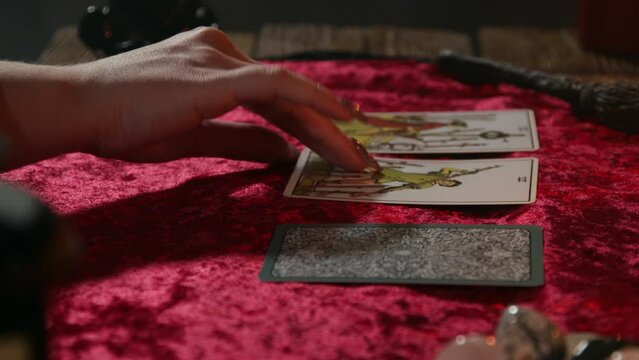 The fortune teller's hand turns over three tarot cards lying on a burgundy tablecloth.