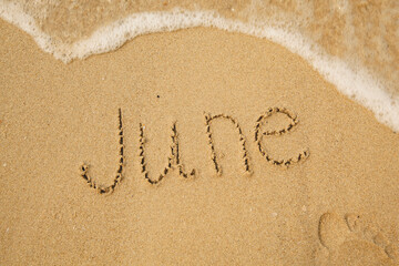 June - handwritten on the soft beach sand with a soft lapping wave.
