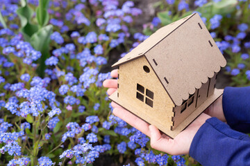 Small wooden house in hands over a flower bed