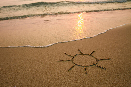 Sun - drawing on the soft beach sand with a soft lapping wave.