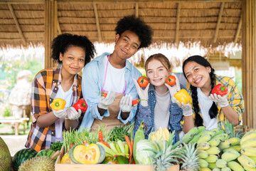 Portrait of smiling teenage girl and boy standing and holding vegetables on fruit stall with fresh vegetables grown in family garden.