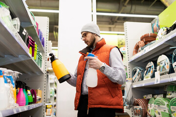 a man in a garden center chooses a new sprayer and sprayer comparing different models