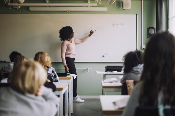 Side view of teacher explaining mathematics to students on white board in classroom