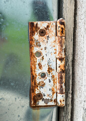 Close-up view of an old rusty hinge on aluminium door.