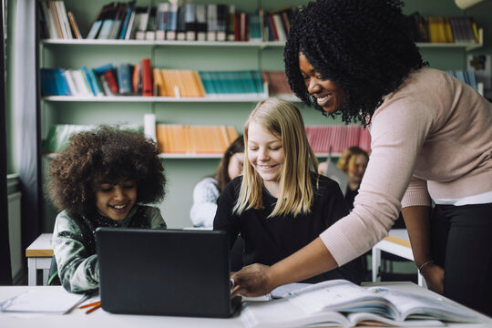 Happy multiracial students and teacher doing e-learning in classroom
