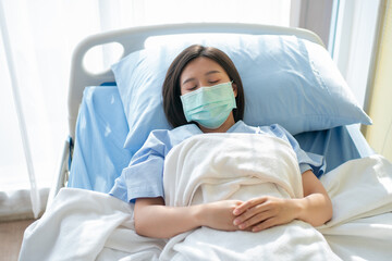 Obraz na płótnie Canvas Sad Asian patient woman lying on the hospital bed and wearing a face mask to protect coronavirus. Concept of Health care, quarantine coronavirus (COVID-19), and Health insurance.