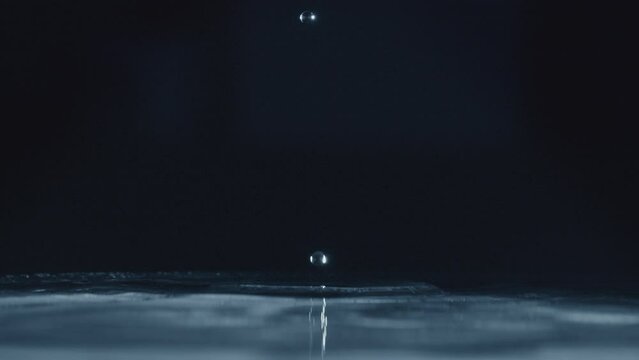 Ultra slow motion close up of water drop falling on a water surface with black background. 4k uhd.