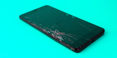 A mobile phone with a broken screen lies on a blue background. A broken smartphone. Electronic gadget in need of repair. Banner for insertion into site. Horizontal image.
