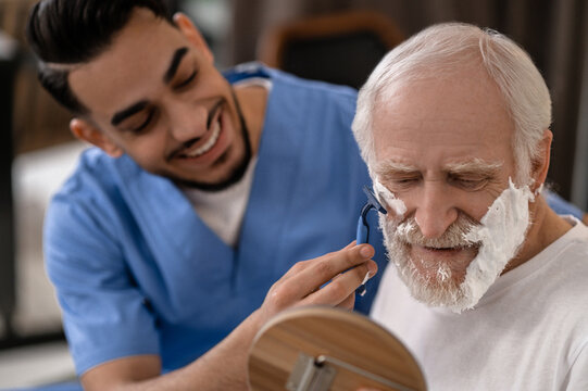 Cheerful Volunteer Giving An Elderly Person A Shave
