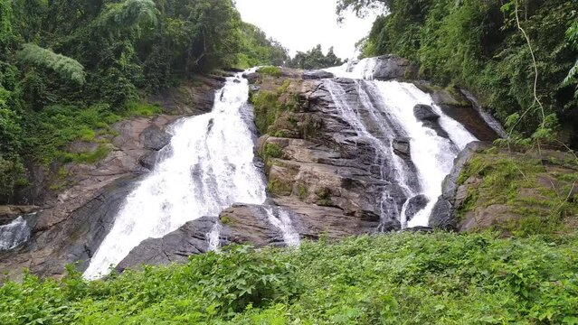 Big wide waterfall stream of fresh water drops falling down and flowing through jungle mountain rocks on wild green forest tree background. Beautiful close up side view. 4k loop high resolution video.