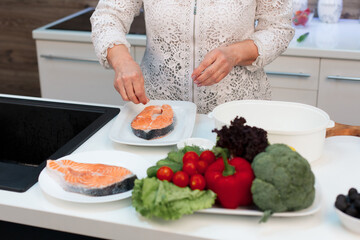 Grandma in a white blouse makes a salmon steak, salts it and adds spices, only hands in the frame