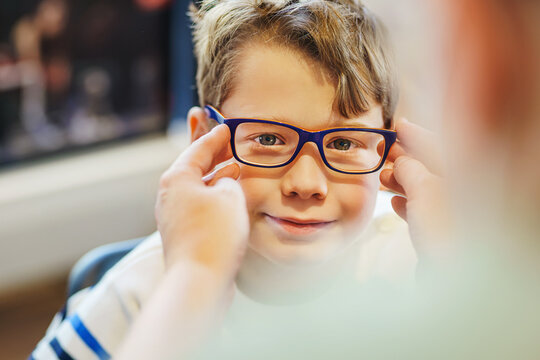  ophthalmologist trying eyeglasses on smiling boy in optics store, banner.