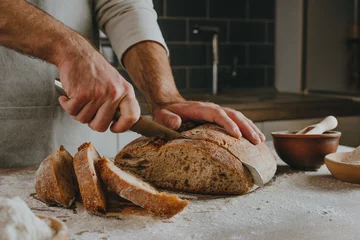 Gordijnen Jonge man in schort die zelfgebakken brood snijdt © lithiumphoto
