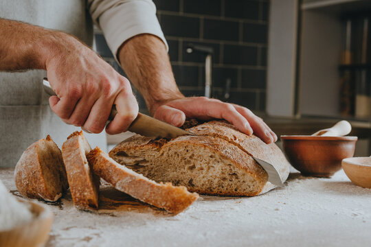 Young man in apron cutting homemade bread