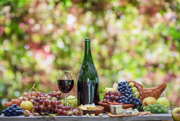 Grapes, bottle of wine and different cheeses on country wooden table and blurred colorful autumn...