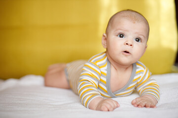 Adorable baby in sunny bedroom. Newborn baby is resting in bed with a warm soft blanket. Family morning at home. Smiling child looking at camera.