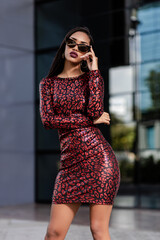 A young Latin American woman in a sexy red dress and sunglasses near a modern building