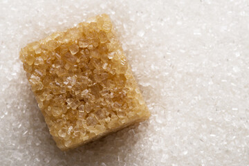 White refined sugar granules and brown sugar cube on it. Food background.