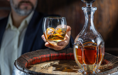 Whisky tasting. Man sits in front of a barrel with a decanter and a glass of whiskey.