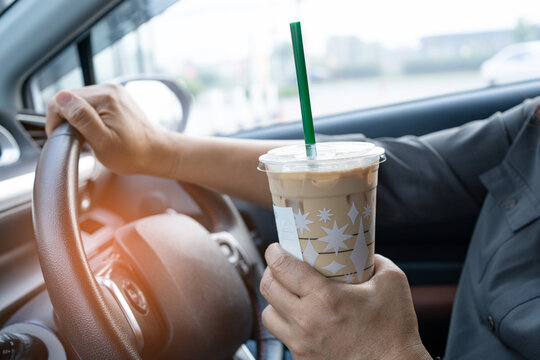 Asian lady holding ice coffee in car dangerous and risk an accident.