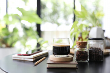 Espresso coffee in a glass cup and notebook and phone and plant pot on black table - obrazy, fototapety, plakaty