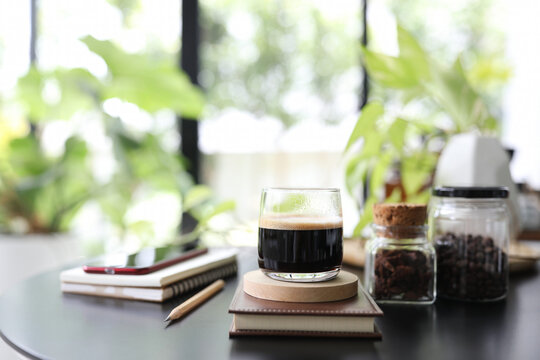 Espresso coffee in a glass cup and notebook and phone and plant pot on black table
