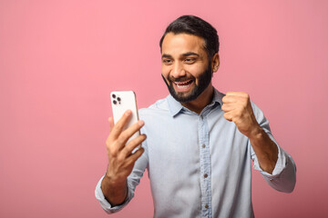 Astonishment Indian man using a smartphone isolated on pink background, hispanic guy looks at the screen with mouth opened holding phone, excited with good deal or unexpected news