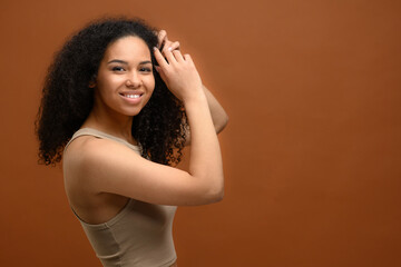 Studio portrait on the brown background of carefree serene multiracial woman looking at camera and laughs. Cheerful peaceful african lady typify self love and body care, charming 20s female