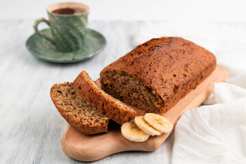 Blurred image of fresh banana bread on a board, in the background a cup of coffee on a light table.
