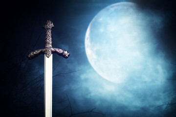 photo of knight sword over dark sky and the moon background. Medieval period concept
