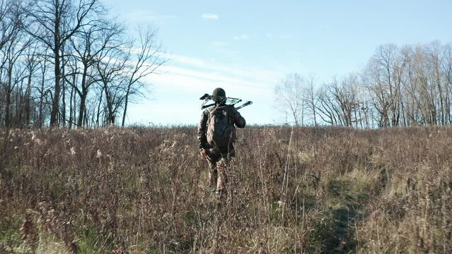 Gimbal following bowhunter wearing camouflage outfit, walking off trail holding bowhunting equipment