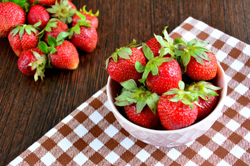 strawberries in fruit bowl on plaid kitchen towel, close-up