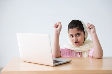 muslim girl using a laptop computer and raised hand for celebrating good news on the table