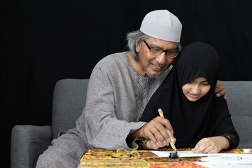 muslim father teaching his daughter about practicing writing arabic with bamboo pens from black ink on paper