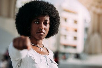 Portrait of a young black woman with afro hair gesturing with her clenched fist symbolizing...