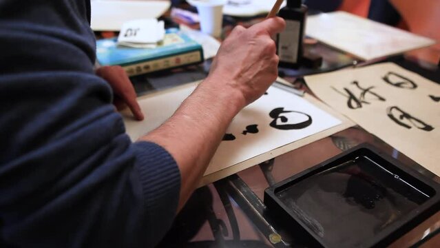 Close-up of a hand and a calligraphy brush. A man writes with a calligraphic brush with black ink on a white sheet of paper the phrase - every day is a good day