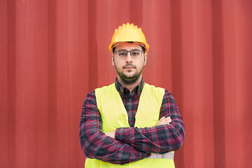 Young dockworker man looking on camera with container in background