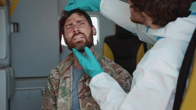 Medic treating wounds of injured soldier suffering in pain. Footage of doctor working under fire. Military officer wounded by gunshots. Ambulances for evacuations. Efforts of military medics. War