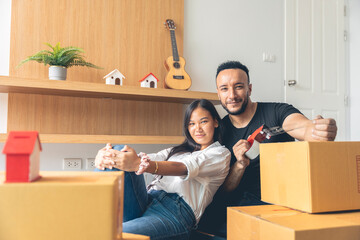 An Asian and Caucasian couple are packing boxes to move house, where they live happily using tape to seal the boxes in preparation for moving.