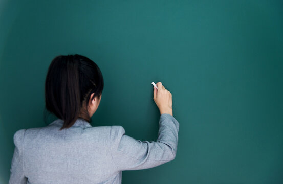 Rear view of young businesswoman on blank chalkboard