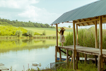 Young woman standing on the wooden pier at the calm lake