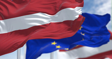 Detail of the national flag of Latvia waving in the wind with blurred european union flag in the background - obrazy, fototapety, plakaty