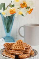 Heart shapet belgian waffles on a plate on the table with white daffodils.